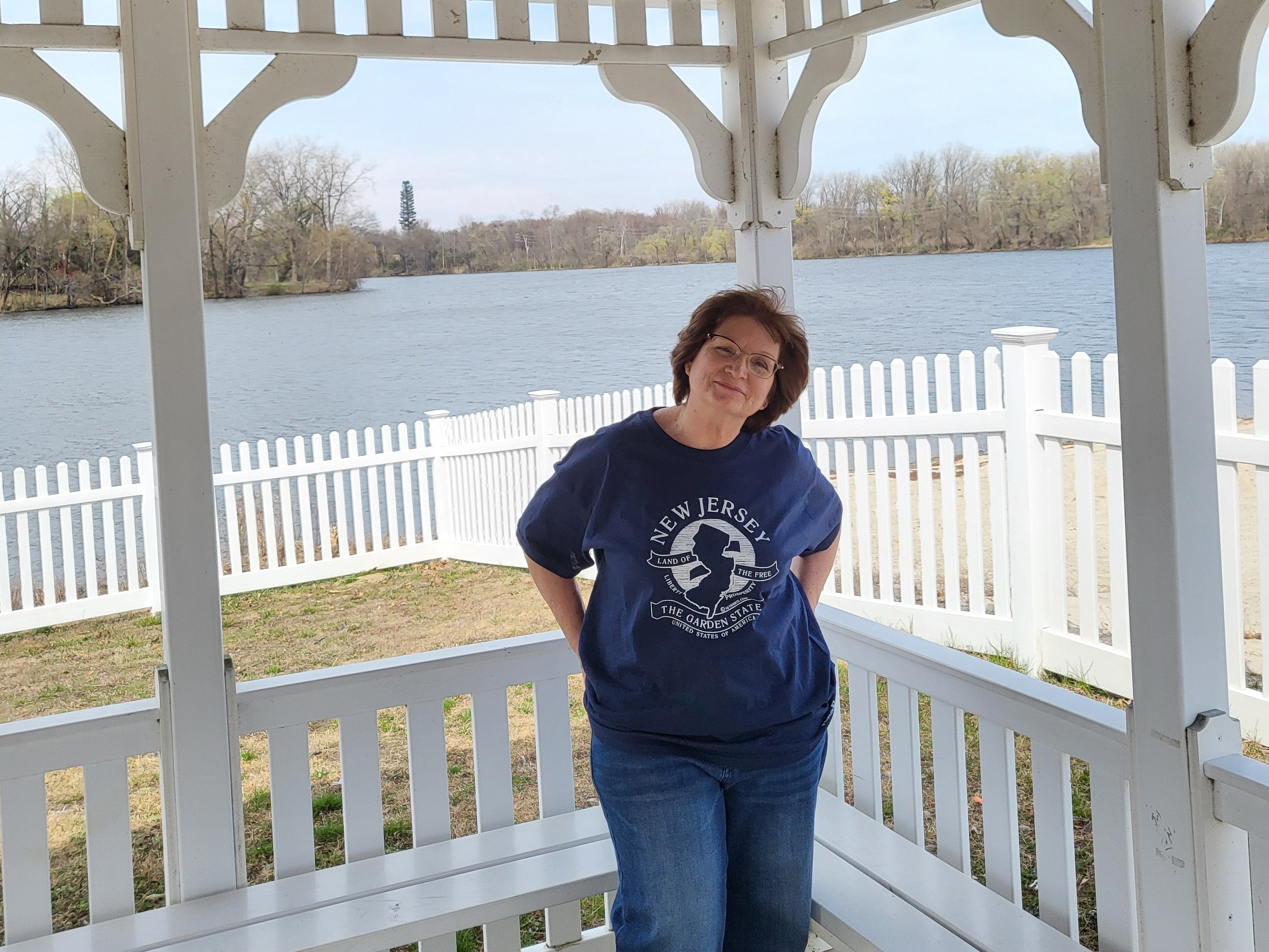 Woman standing on a porch with a scenic view of a lake and trees.
