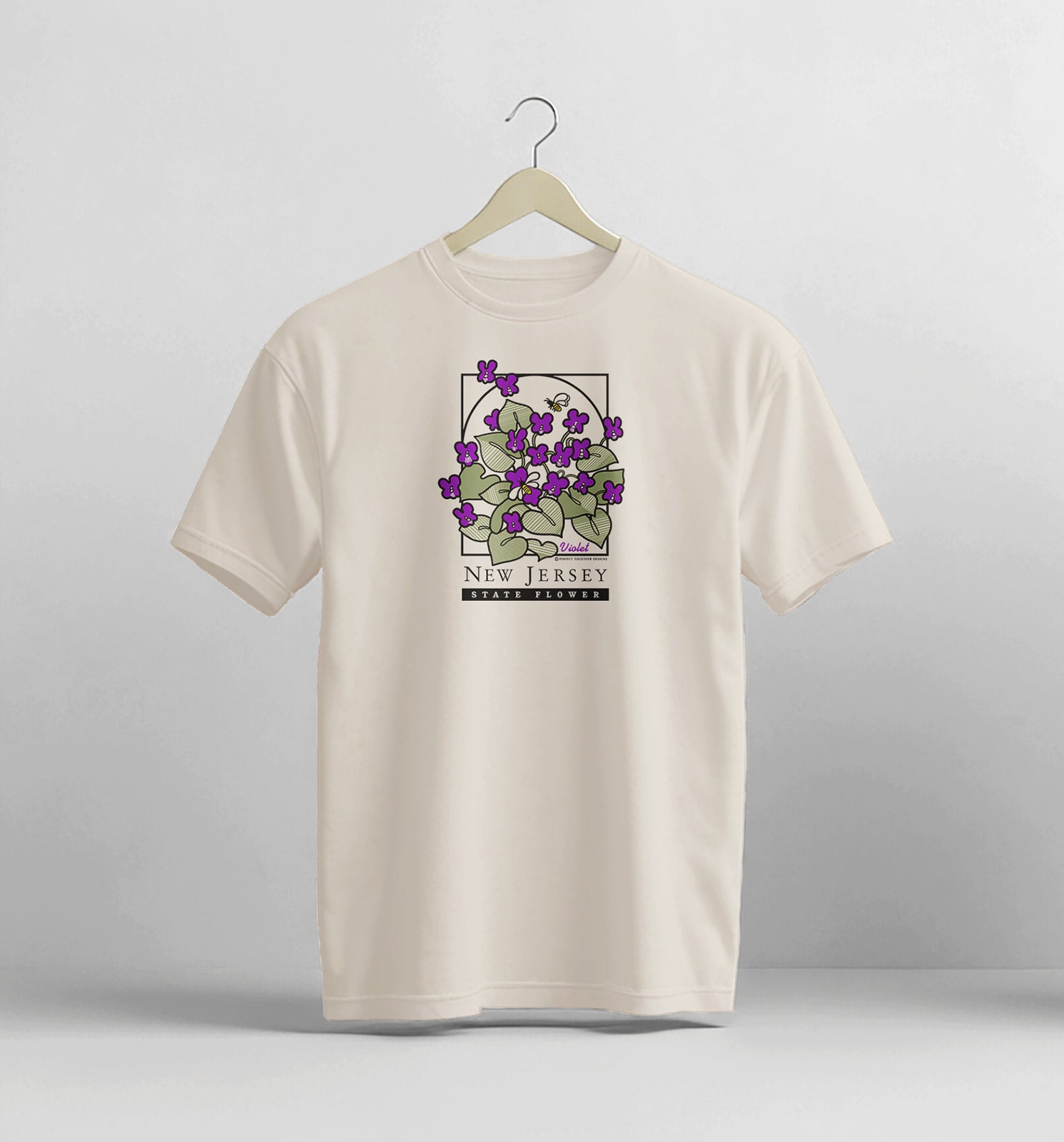 Beige t-shirt with a graphic design of purple flowers on a hanger against a light gray background
