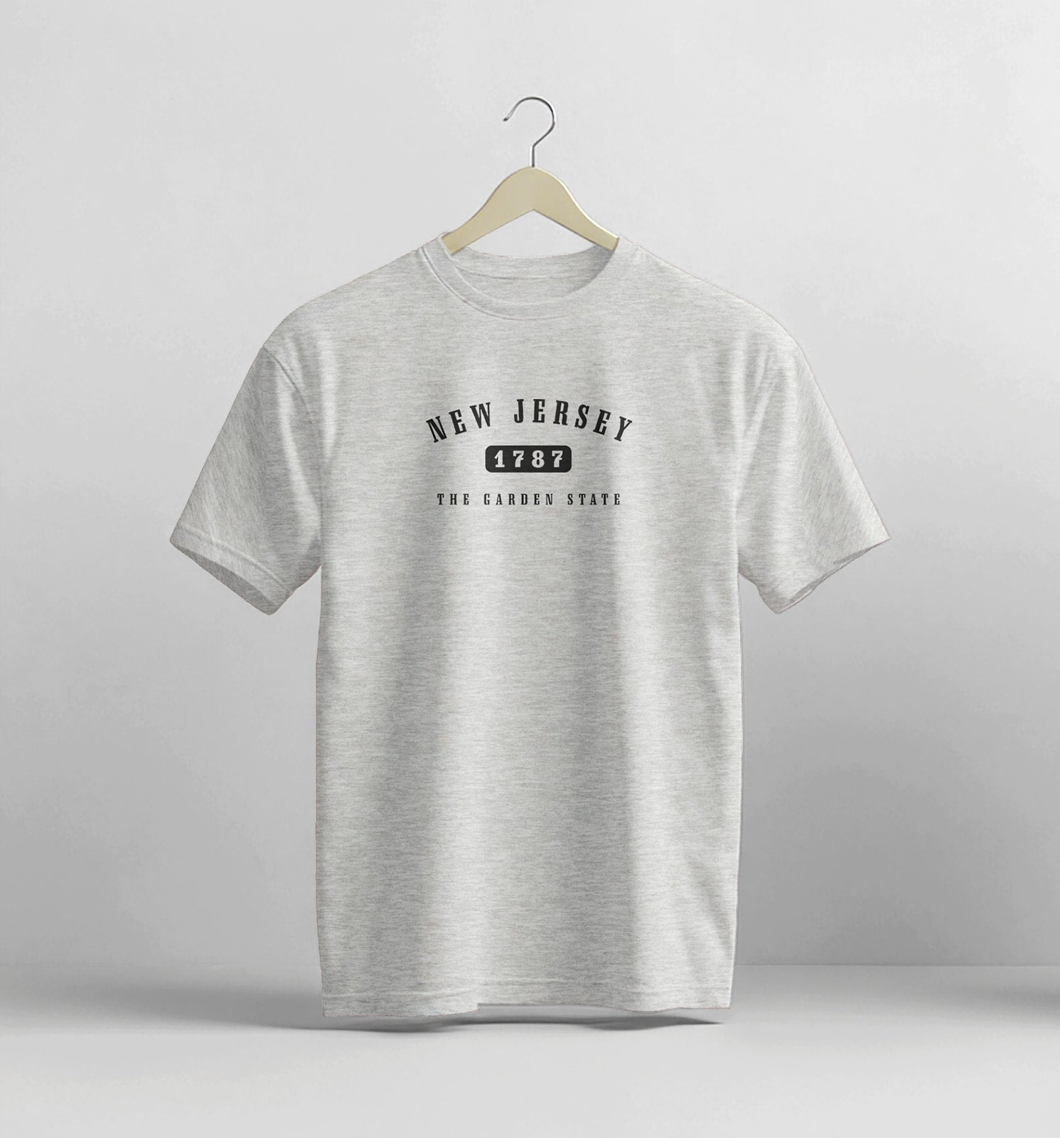 Gray t-shirt with 'New Jersey 1787' text on a hanger against a light gray background