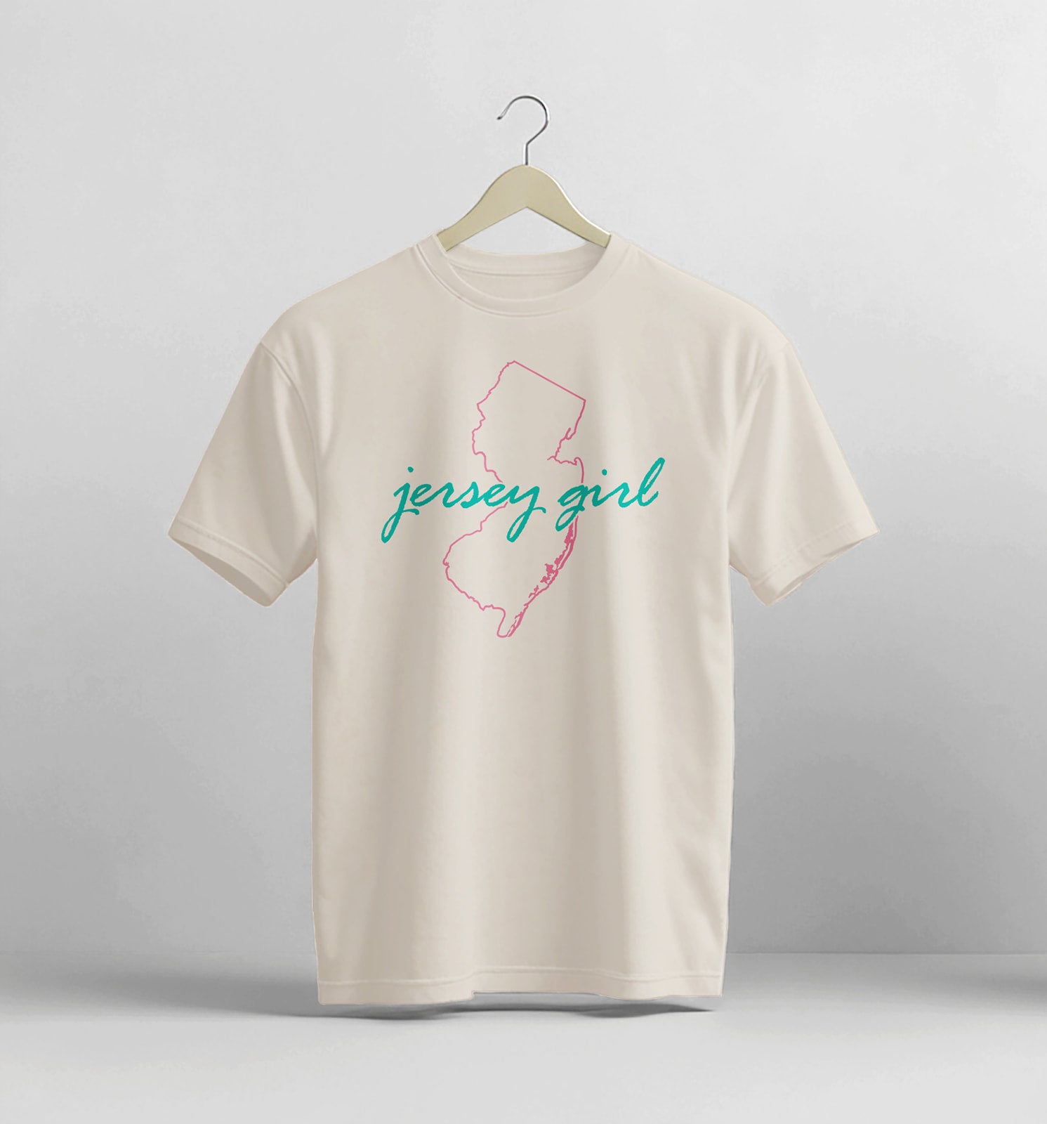 Beige t-shirt with 'jersey girl' design on a hanger against a light gray background