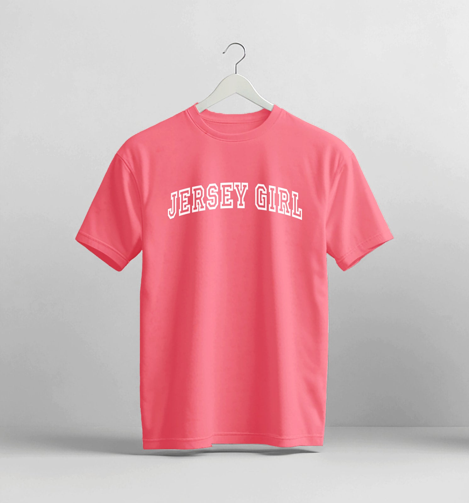 Pink t-shirt with 'Jersey Girl' text on a hanger against a gray background