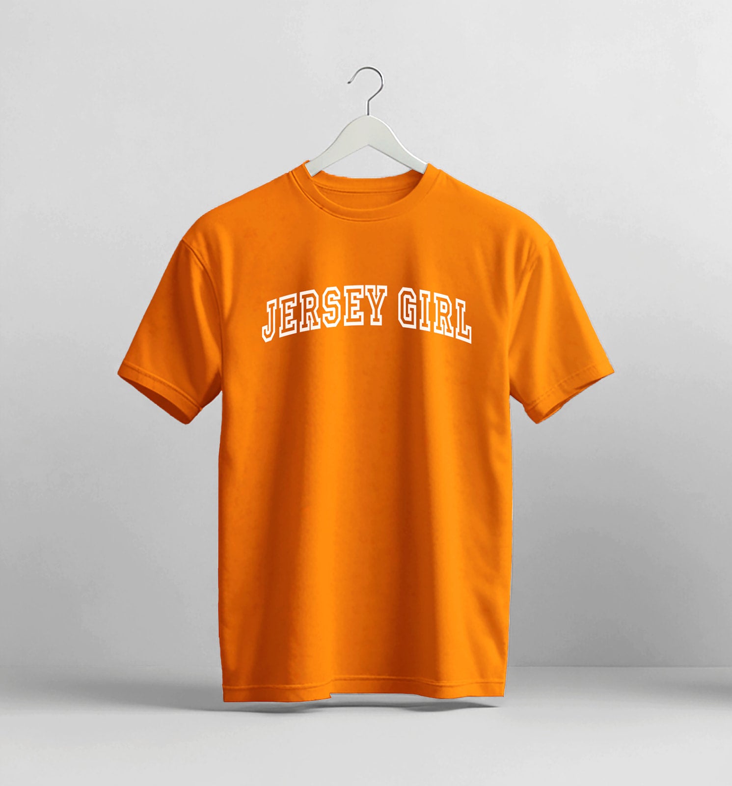 Orange t-shirt with 'Jersey Girl' text on a hanger against a gray background