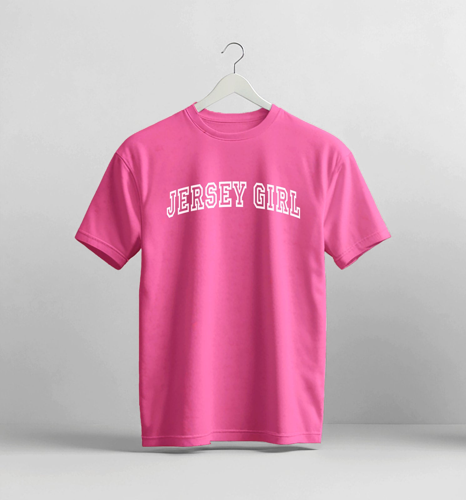 Pink t-shirt with 'Jersey Girl' text on a hanger against a gray background