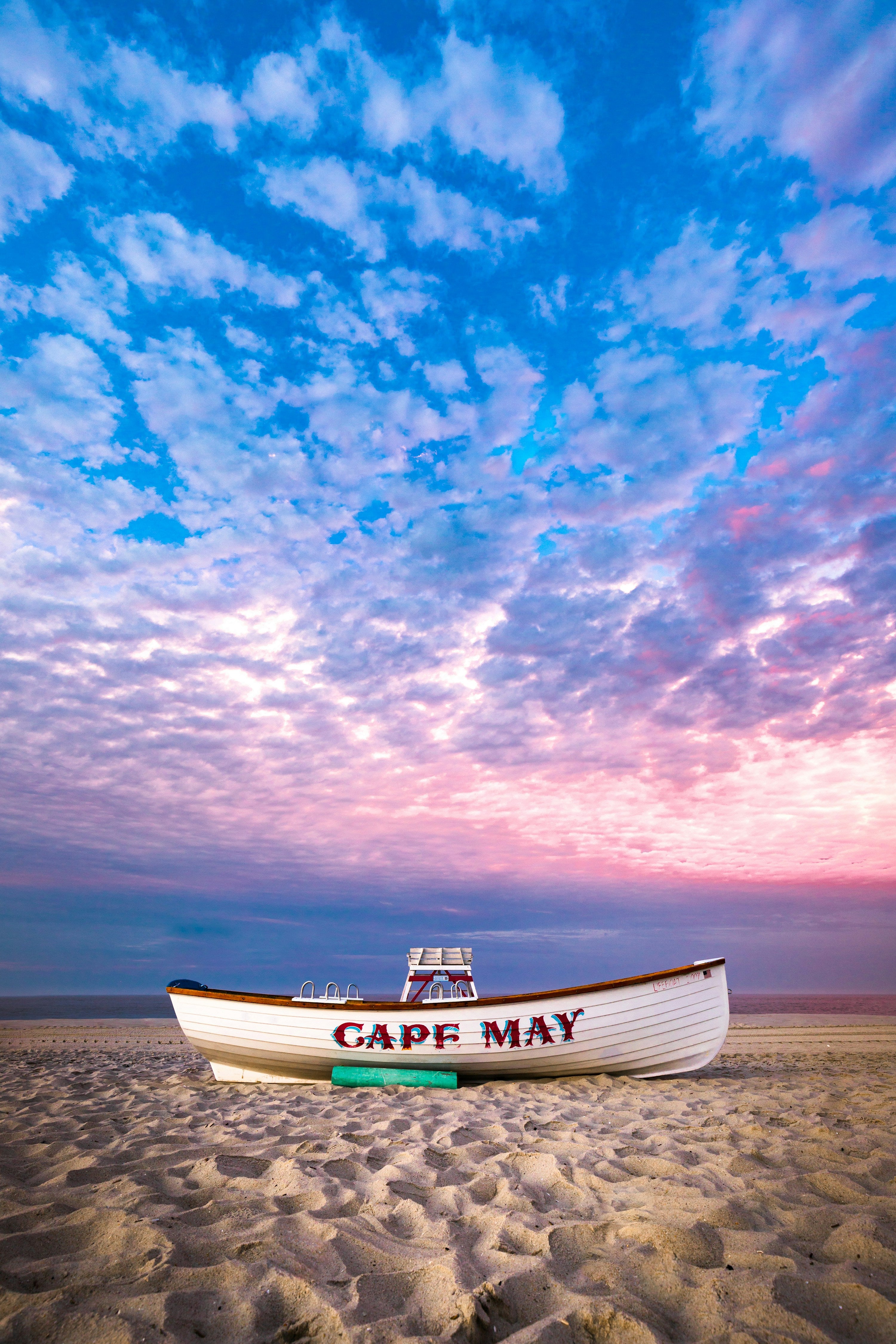 Boat on a beach with 'Cape May' written on it, under a colorful sky.